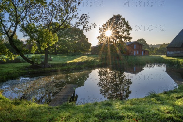 Manor with historic stables and pond, from 1923, in backlight with sun star, Gut Othenstorf, Mecklenburg-Western Pomerania, Germany