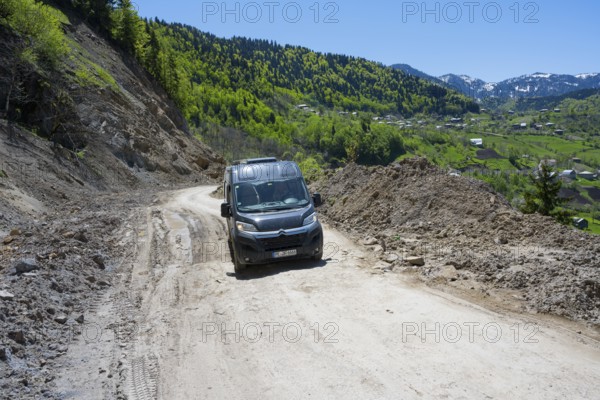 A van drives on a winding mountain road surrounded by wooded hills under blue skies, campers on the way to Goderdzi Pass, Ajara region, Adjara, autonomous republic, Georgia