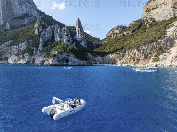 Motor boat off picturesque rocky coast, cliffs with L'Aguglia pinnacle, blue sea and Cala Goloritzé beach, aerial view, Golfo di Orosei, Baunei, Sardinia, Italy
