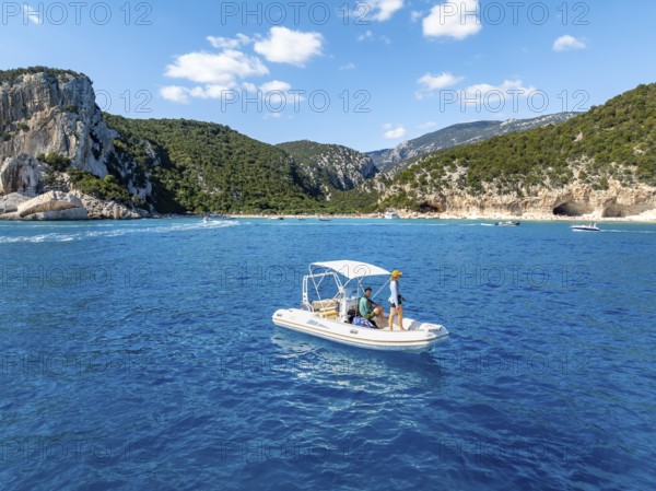 Motor boat off picturesque rocky coast, cliffs and Cala Luna beach, aerial view, Golfo di Orosei, Baunei, Sardinia, Italy
