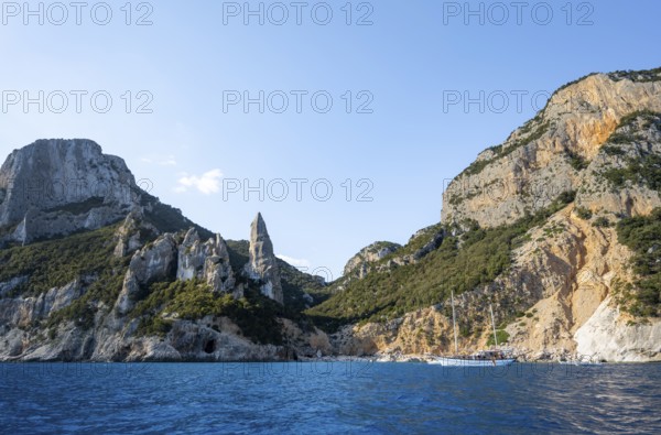 Excursion boat off picturesque rocky coast, cliffs in morning light, L'Aguglia pinnacle, blue sea and Cala Goloritzé beach, Golfo di Orosei, Baunei, Sardinia, Italy