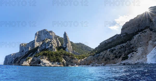 Picturesque rocky coast, cliffs with L'Aguglia pinnacle, blue sea and Cala Goloritzé beach, sun star, Golfo di Orosei, Baunei, Sardinia, Italy