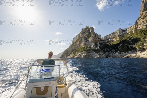 Young man rides a motorboat along the picturesque rocky coast, cliffs and blue sea, Golfo di Orosei, Baunei, Sardinia, Italy