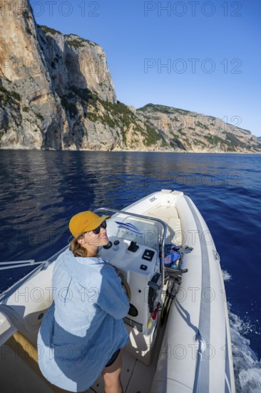 Young woman riding a motorboat along the picturesque rocky coast, cliffs and blue sea, Golfo di Orosei, Baunei, Sardinia, Italy
