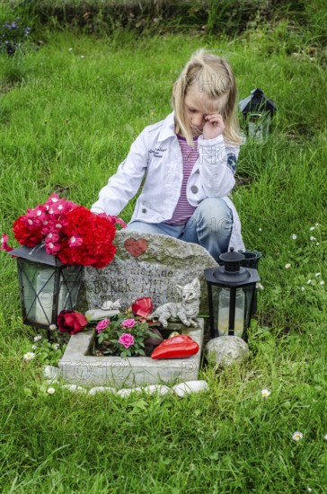 Grieving blonde 7-year-old girl at her cat's grave at pet cemetery in Ystad, Skåne County, Sweden, Scandinavia