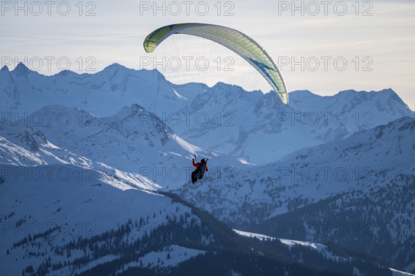 Paragliders flying over snowy mountain peaks in winter in evening light, Kitzbühel Alps, Tyrol, Austria
