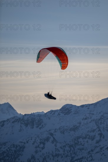 Paragliders flying over snowy mountain peaks in winter in evening light, Kitzbühel Alps, Tyrol, Austria