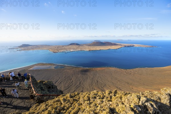 View of La Graciosa island with volcanic craters in the evening light, tourists on an observation deck at the Mirador del Río viewpoint designed by artist César Manrique, Lanzarote, Canary Islands, Spain