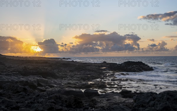 Dramatic cloudy sky with sunbeams at sunset, seaside coast with volcanic rocks, La Santa, Lanzarote, Canary Islands, Spain