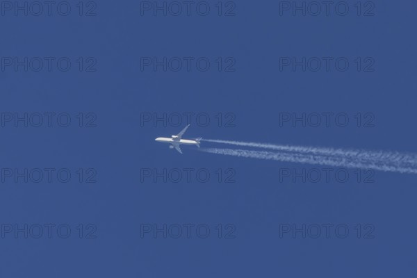 Jet passenger aircraft flying in a blue sky with contrails or vapour trails behind, England, United Kingdom