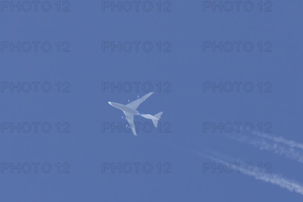 Boeing 747 jumbo jet cargo aircraft flying in a blue sky with contrails or vapour trails behind, England, United Kingdom