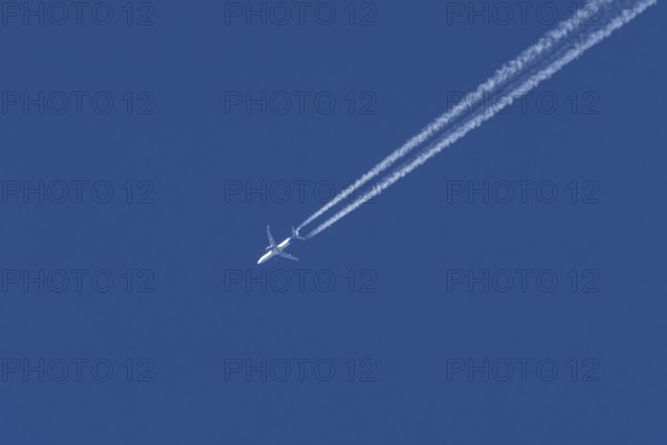 Jet passenger aircraft flying in a blue sky with contrails or vapour trails behind, England, United Kingdom