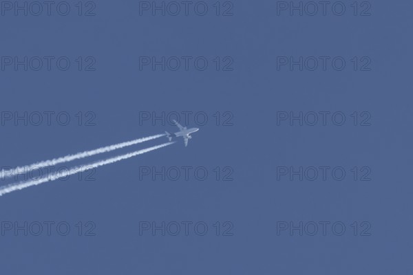 Airbus jet passenger aircraft flying in a blue sky with contrails or vapour trails behind, England, United Kingdom