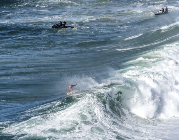 Surfers with their jet ski pilots in the Atlantic waves below Farol de Nazaré, Forte São Miguel, known as a surfer hot spot with monster waves between November and February of each year, Nazaré, Portugal