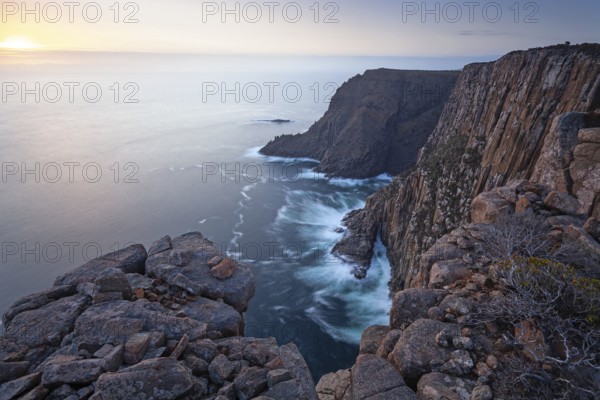 Long exposure shows sunset over the cliffs of Cape Raoul. Golden light hits the sea and colors the rocks warmly in the evening. Cape Raoul, Tasman Peninsula, Tasmania, Australia