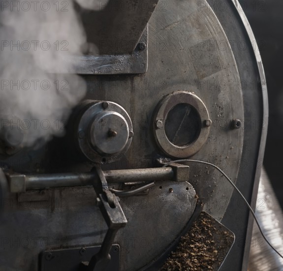 Machine for roasting coffee beans called roaster with a special automatic mixing device at work in a production room