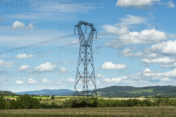 High voltage power lines against a bright blue sky with scattered clouds, Puy de Dome, Auvergne Rhone Alpes, France