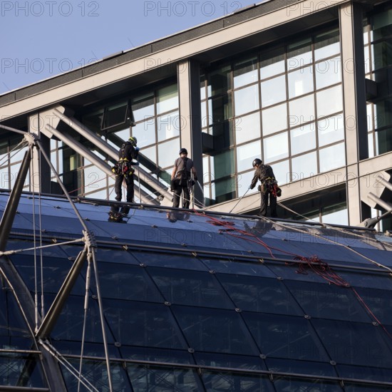 Three male glass cleaners abseiling down a glass roof of Berlin Central Station to clean windows, Berlin, Germany