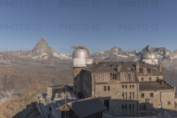 This breathtaking view shows the iconic Matterhorn mountain rising behind a historic observatory building. The clear blue sky enhances the serene atmosphere in autumn