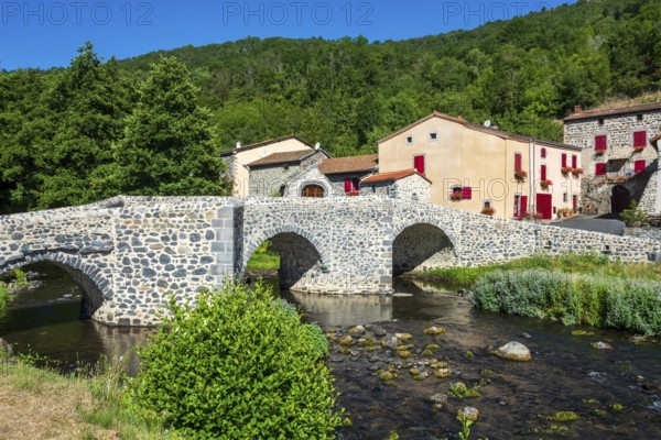 Stone bridge over the Pavin couze river flowing through the village of Saurier, Puy de Dome. Auvergne Rhone Alpes, France