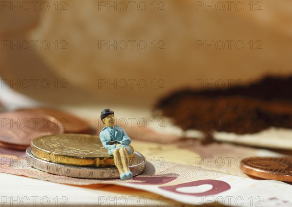 Miniature figure of a woman sitting on coins and banknotes, ground coffee in a filter bag in the background, North Rhine-Westphalia, Germany
