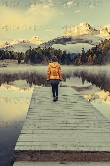 Young woman at Lake Staz near Sankt Moritz in the Engadine in Switzerland. Morning atmosphere with fog in autumn. Reflection of water