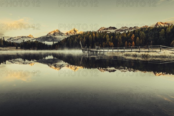 Lake Staz near Sankt Moritz in the Engadin in Switzerland. Morning atmosphere with fog in autumn. Water reflection and snow-covered mountains in the background