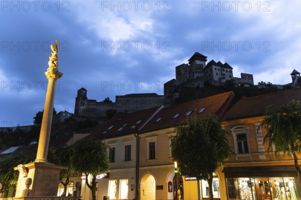 Night shot of the plague column column commemorating the victims of the plague at the beginning of the 18th century, in the background is Trencín Castle, Capital of Culture 2026, Trencín, Slovakia