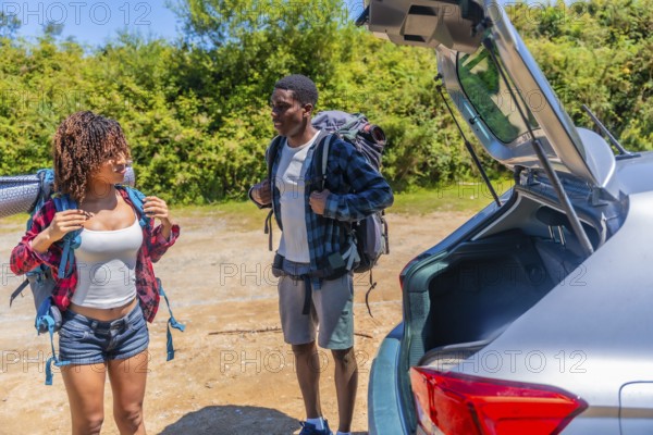 Young couple preparing backpacks next to their car before starting a hiking trip in the nature