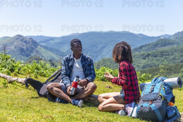 Two hikers taking a break from their trek, enjoying drinks amidst a picturesque mountain landscape