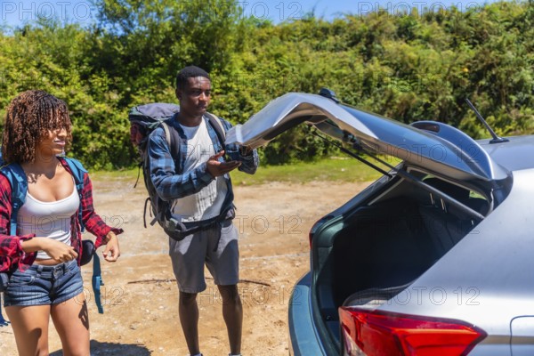 Young couple of hikers preparing their backpacks for an exciting road trip, opening the car trunk amidst stunning mountain scenery
