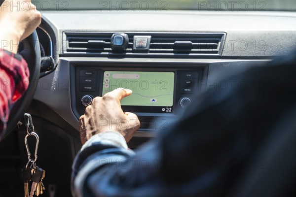 Close up of passenger using navigation system on car dashboard while driver operates steering wheel