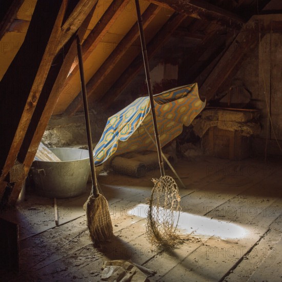 Sunlight filters through an attic, illuminating a colorful sunshade and a butterfly net alongside dust-covered wooden beams, creating a tranquil, nostalgic atmosphere
