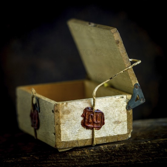 A wooden box is secured with twine, featuring a deep red wax seal that signifies authenticity and quality. The warm tones highlight traditional craftsmanship and care in presentation