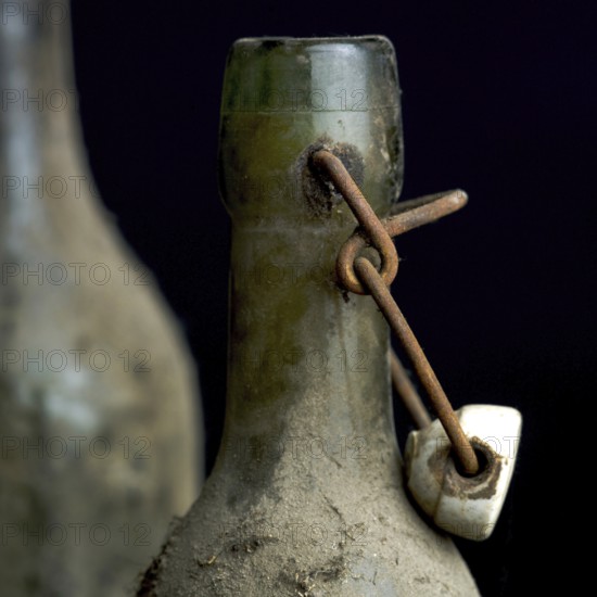 Three dusty vintage bottles stand together, covered in grime, highlighting their age and history. These relics evoke memories of past gatherings and forgotten stories in a dimly lit cellar