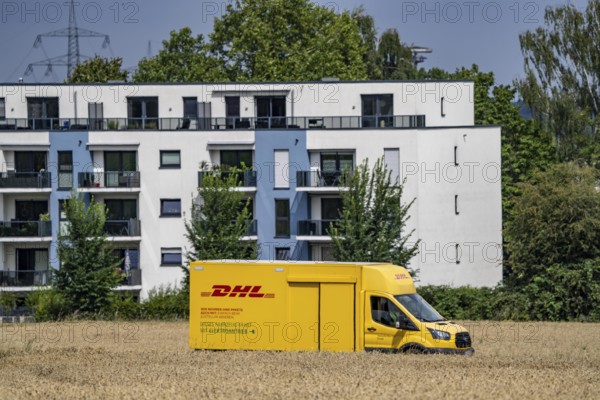 DHL parcel van, electric vehicle, on the way to a customer, rural, driving along a dirt track through a corn field, North Rhine-Westphalia, Germany