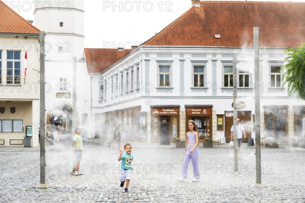 Water mist system in the city centre of Trencin, children use the refreshment in the summer heat, Trencín, Slovakia
