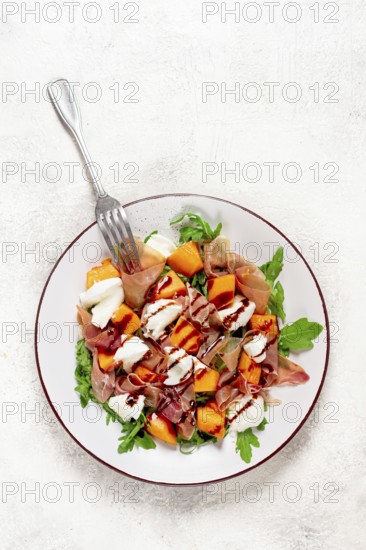 Salad with slices of ripe melon, prosciutto, mozzarella and fresh arugula, decorated with balsamic glaze