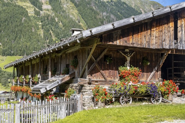Colourful floral decorations and crucifix at a rustic alpine hut, Ridnauntal, South Tyrol, Italy