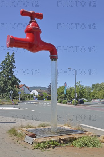 Red free-standing tap with water jet, fountain, modern art, sculpture, dummy, figure, pipeline, pipe, water pipe, water, illusion, deceive, floating, surreal, free-standing, without, no, none, missing, loose, unconnected, not, separate, detached, hanging, oversized, XXL, funny, amusing, humorous, comical, symbol, water supply, drinking water, Oberstedten, Oberursel, Taunus, Hesse, Germany