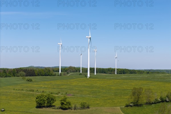 Wind turbines stand on a green area, surrounded by trees under a clear sky, Swabian Alb, Baden-Württemberg, Germany