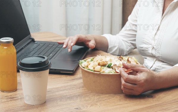 A woman is working on a laptop at home, there is food on the table, salad, coffee and juice, delivery, work at home