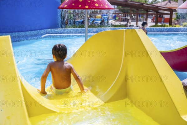 Young boy enjoying a thrilling ride down a vibrant waterslide at a lively water park, embracing the excitement of summer vacation