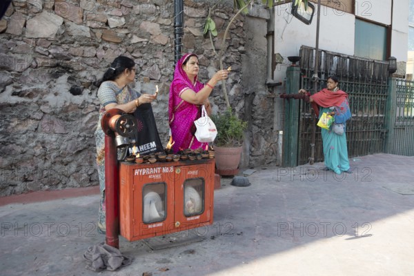 Indian woman holding tea lights in the air at a fire hydrant, Govind Dev Ji Hindu temple in the old city centre, Jaipur, Rajasthan, India