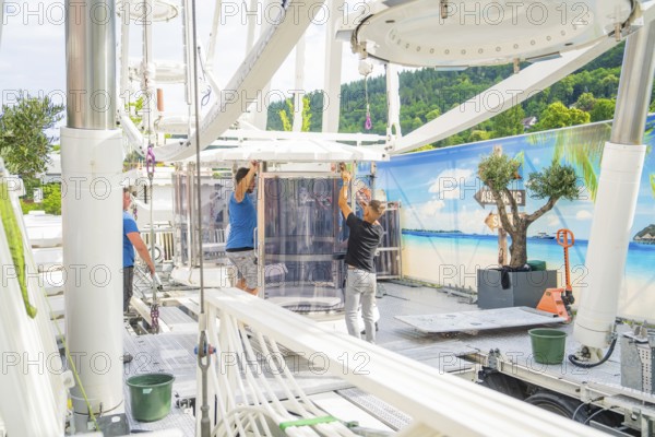 People aligning a cabin in a Ferris wheel in front of a landscape scenery, Ferris wheel construction for the 950th anniversary of the town of Calw, Black Forest, Germany