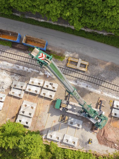 Crane on construction site on railway tracks, concrete blocks laid out next to a green forest landscape, construction of the Hermann Hesse railway, Calw, Germany