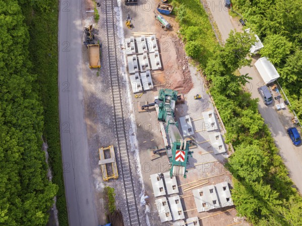 Aerial view of a construction site on railway tracks surrounded by forest with a green crane, construction of the Hermann Hesse railway, Calw, Germany
