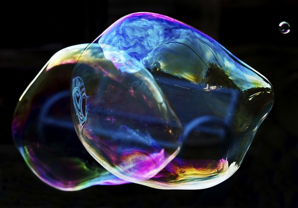 Irregular, iridescent soap bubble in the colours of the rainbow against a black background, Recklinghausen, Germany