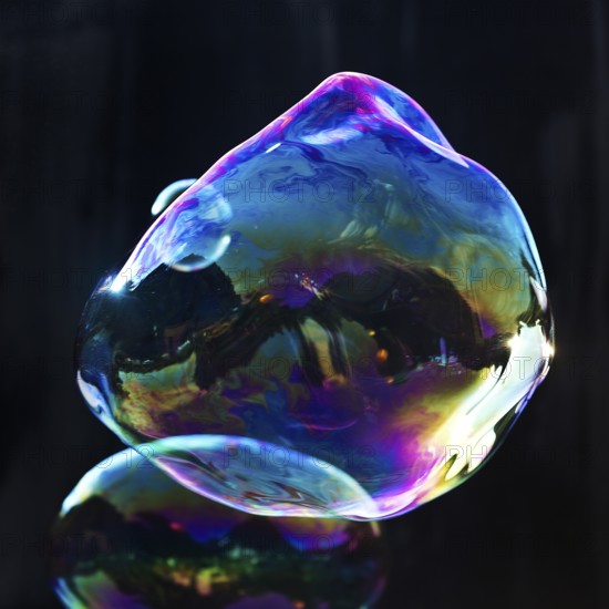 Large, irregular, iridescent soap bubbles in the colours of the rainbow against a black background, Recklinghausen, Germany