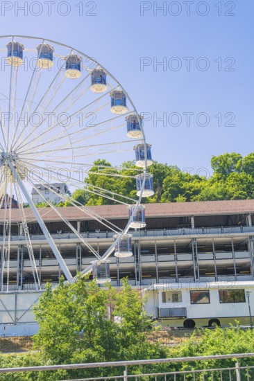 A large Ferris wheel towers over a building, surrounded by green trees under a clear blue sky, 950 years Calw, Germany